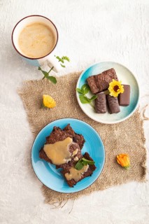 Chocolate brownie with caramel sauce with a cup of coffee on gray concrete background and linen