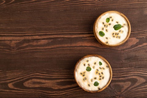Yoghurt with granadilla and mint in wooden bowl on brown wooden background. top view, flat lay,