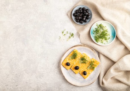 Marble cheese with olives and watercress microgreen on gray concrete background and linen textile.