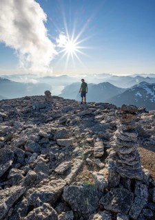 Mountaineer on the summit of Skala with cairn, view of mountain landscape and fjord Faleidfjorden,