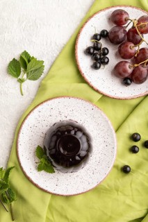 Black currant and grapes jelly on gray concrete background and green linen textile. top view, flat