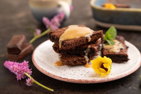 Chocolate brownie with caramel sauce with a cup of coffee on black concrete background. side view,