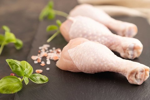 Raw chicken legs with herbs and spices on a black slate cutting board on a black concrete