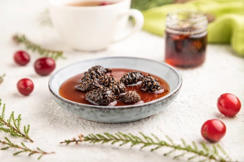 Pine cone jam with herbal tea on gray concrete background and green linen textile. Side view,