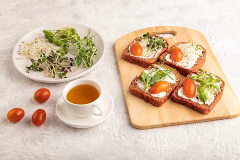 Red beet bread sandwiches with cream cheese, tomatoes and microgreen on gray concrete background.