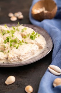 Stewed chicken fillets with coconut milk sauce and rucola microgreen on black concrete background