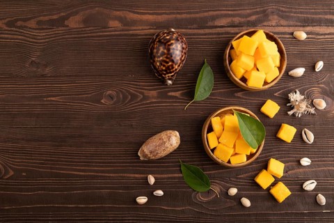 Dried and candied mango cubes in wooden bowls on brown wooden textured background. Top view, flat
