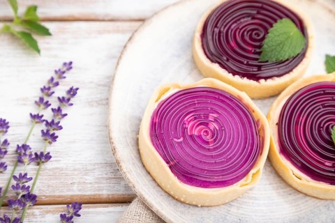 Sweet tartlets with jelly and milk cream with cup of coffee on a white wooden background and linen