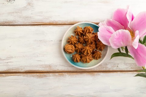 Homemade soft caramel fudge candies on blue plate on white wooden background, peony flower