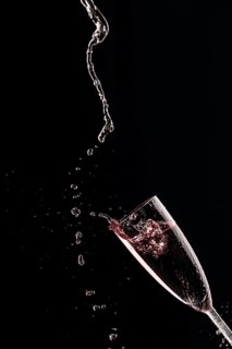 Drops and splashes fly from a champagne glass with rose sparkling wine on a black background