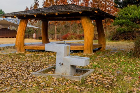 Concrete water fountain in front of covered picnic shelter in public roadside park