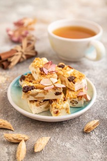 Traditional candy nougat with nuts and sesame with cup of green tea on brown concrete background.
