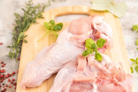 Raw turkey wing with herbs and spices on a wooden cutting board on a brown concrete background.