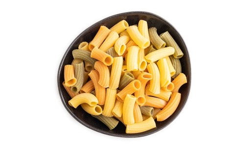 Rigatoni colored raw pasta in bowl isolated on white background. Top view, flat lay