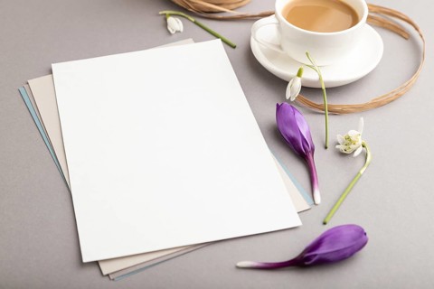 White paper sheet mockup with spring snowdrop crocus and galanthus flowers and cup of coffee on