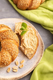 Homemade sweet bun with peanut butter and cup of coffee on a gray concrete background and green