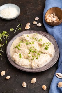 Stewed chicken fillets with coconut milk sauce and rucola microgreen on black concrete background