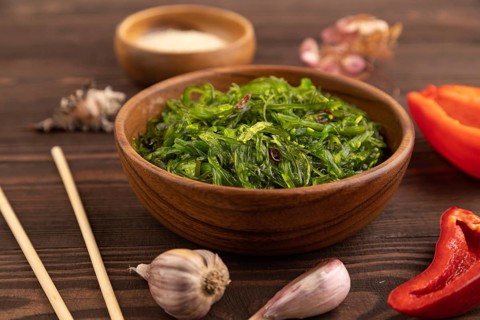 Chuka seaweed salad in wooden bowl on brown wooden background. Side view, close up, selective focus