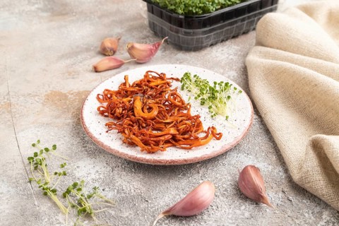 Fried Cordyceps militaris mushrooms on brown concrete background with microgreen, herbs and spices.