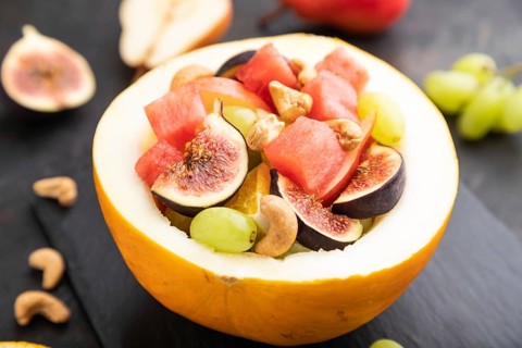 Vegetarian fruit salad of watermelon, grapes, figs, pear, orange, cashew on slate board on a black