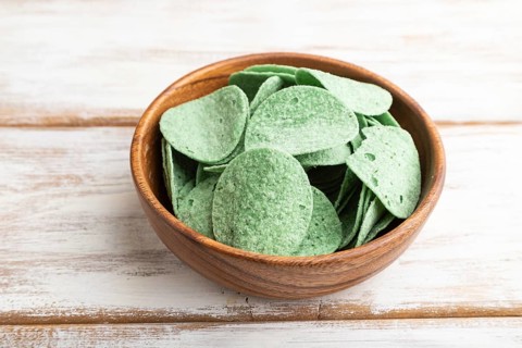Green potato chips with herbs in wooden bowl on white wooden background. Side view, close up