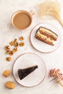 Chocolate biscuit cake with caramel cream and walnuts, cup of coffee on gray concrete background.