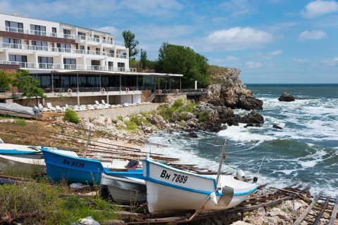 A coastal hotel overlooking the moving sea, surrounded by boats and rocky landscape, harbour and
