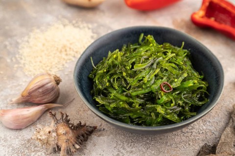 Chuka seaweed salad in blue ceramic bowl on brown concrete background. Side view, close up,