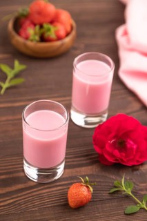 Sweet strawberry liqueur in glass on a brown wooden background and pink textile. side view, close