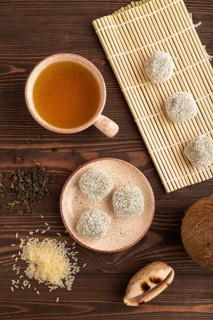 Japanese rice sweet buns mochi filled with pandan and coconut jam and cup of green tea on brown