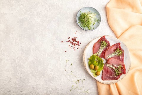 Slices of smoked salted meat with cilantro microgreen on gray concrete background and orange