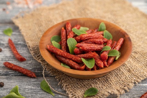 Small smoked sausage with borage microgreen, salt and pepper on gray wooden background and linen