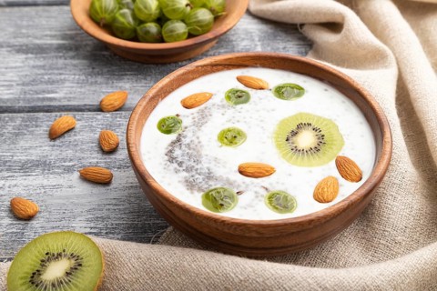 Yogurt with kiwi, gooseberry, chia and almonds in wooden bowl on gray wooden background and linen