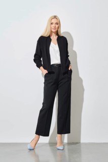 Confident woman in black pantsuit with hands in pockets posing next to white wall