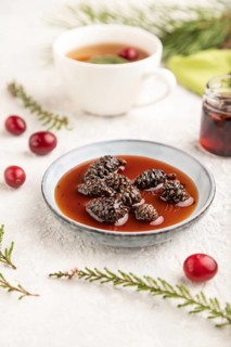 Pine cone jam with herbal tea on gray concrete background and green linen textile. Side view,
