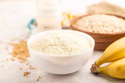 Powdered milk and oatmeal, banana baby food mix, infant formula, pacifier, bottle, spoon on gray