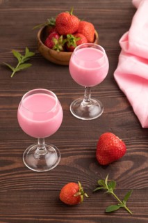 Sweet strawberry liqueur in glass on a brown wooden background and pink textile. side view, close