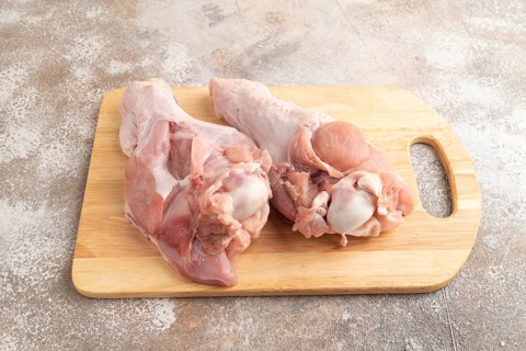 Raw turkey wing with herbs and spices on a wooden cutting board on a brown concrete background.