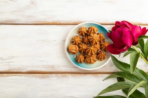 Homemade soft caramel fudge candies on blue plate on white wooden background, peony flower