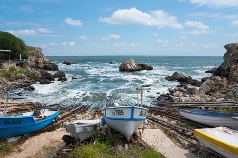 Boats on a coastline with rough seas and rocky outcrops in the background, harbour, Tyulenovo,