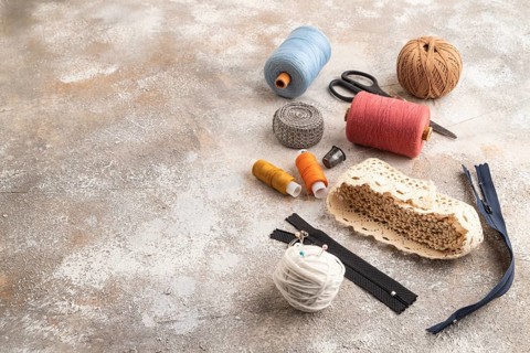 Sewing accessories: scissors, thread, thimbles, braid on brown concrete background. Side view, copy