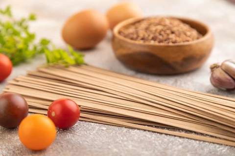 Japanese buckwheat soba noodles with tomato, eggs, spices, herbs on brown concrete background. Side