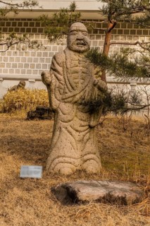 Stone carved statue of Buddhist deity kanakavatsa in front of white wall in garden in South Korea