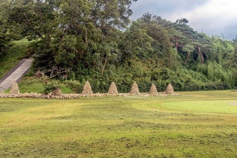 Row of cairn (towers of stack stones) in front of treeline with stairs up side of hill on left in