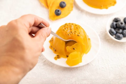 Mango and passion fruit jelly with blueberry on gray concrete background with hand. side view,