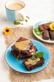 Chocolate brownie with caramel sauce with a cup of coffee on gray concrete background and linen
