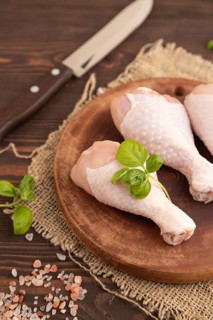 Raw chicken legs with herbs and spices on a wooden cutting board on a brown wooden background and