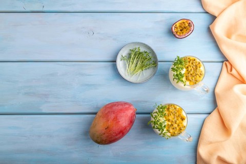 Mango yogurt with passionfruit and cilantro microgreen in glass on blue wooden background with