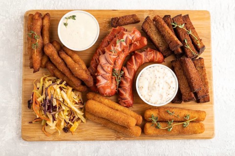 Set of snacks: sausages, nuggets, cheese sticks, toast, cabbage salad on a cutting board on a gray