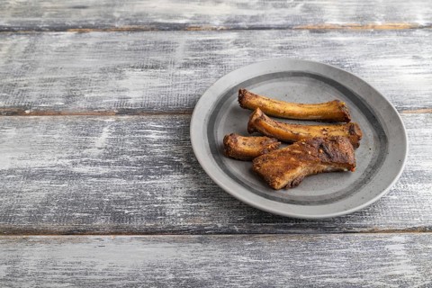 Pork ribs on a wooden plate on a gray wooden background. Side view, close up, copy space